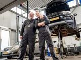 Lachende monteurs met arm over elkaar en auto op de achtergrond