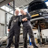 Lachende monteurs met arm over elkaar en auto op de achtergrond