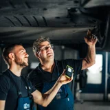 twee Ames Volkswagen monteurs onder een auto met een zaklamp