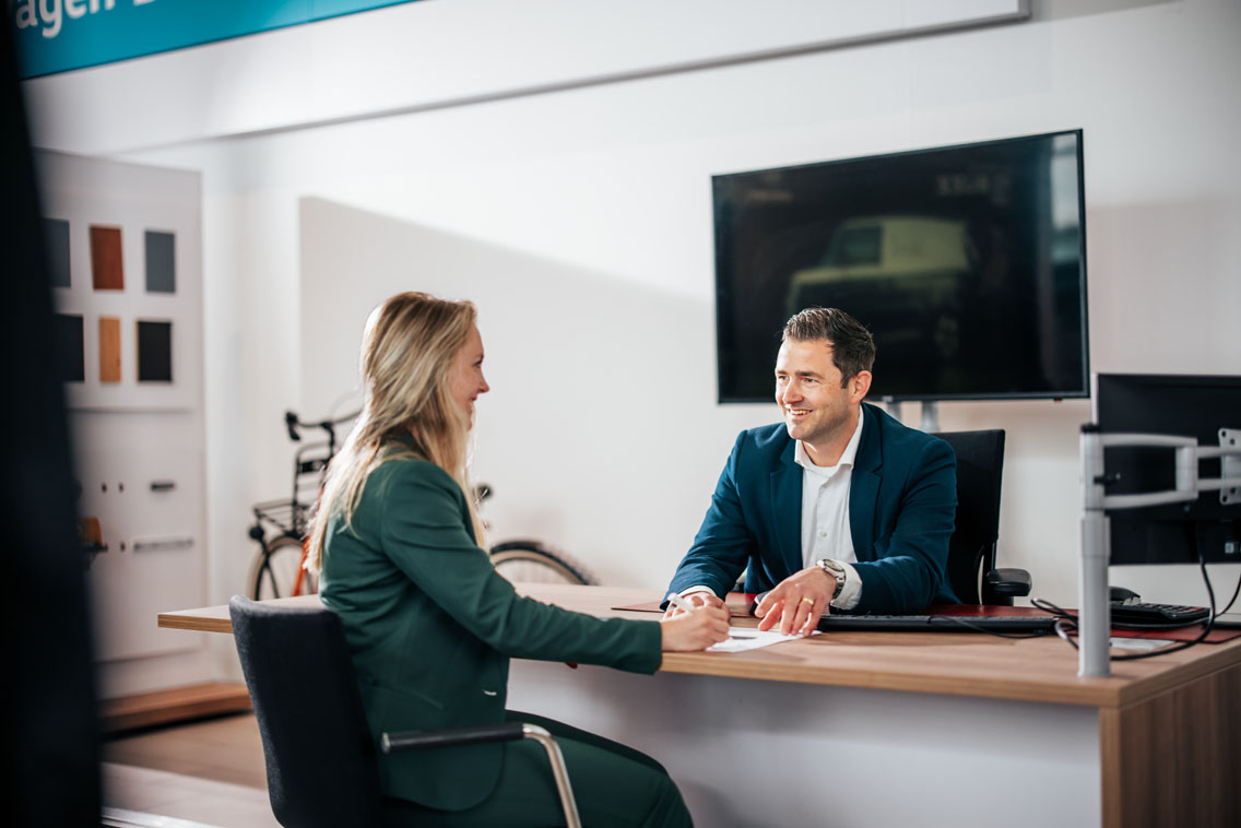 Sales medewerker en klant tekenen een formulier bij een bureau