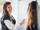 Marketing stagiaire lachend aan het praten met andere vrouw bij white board